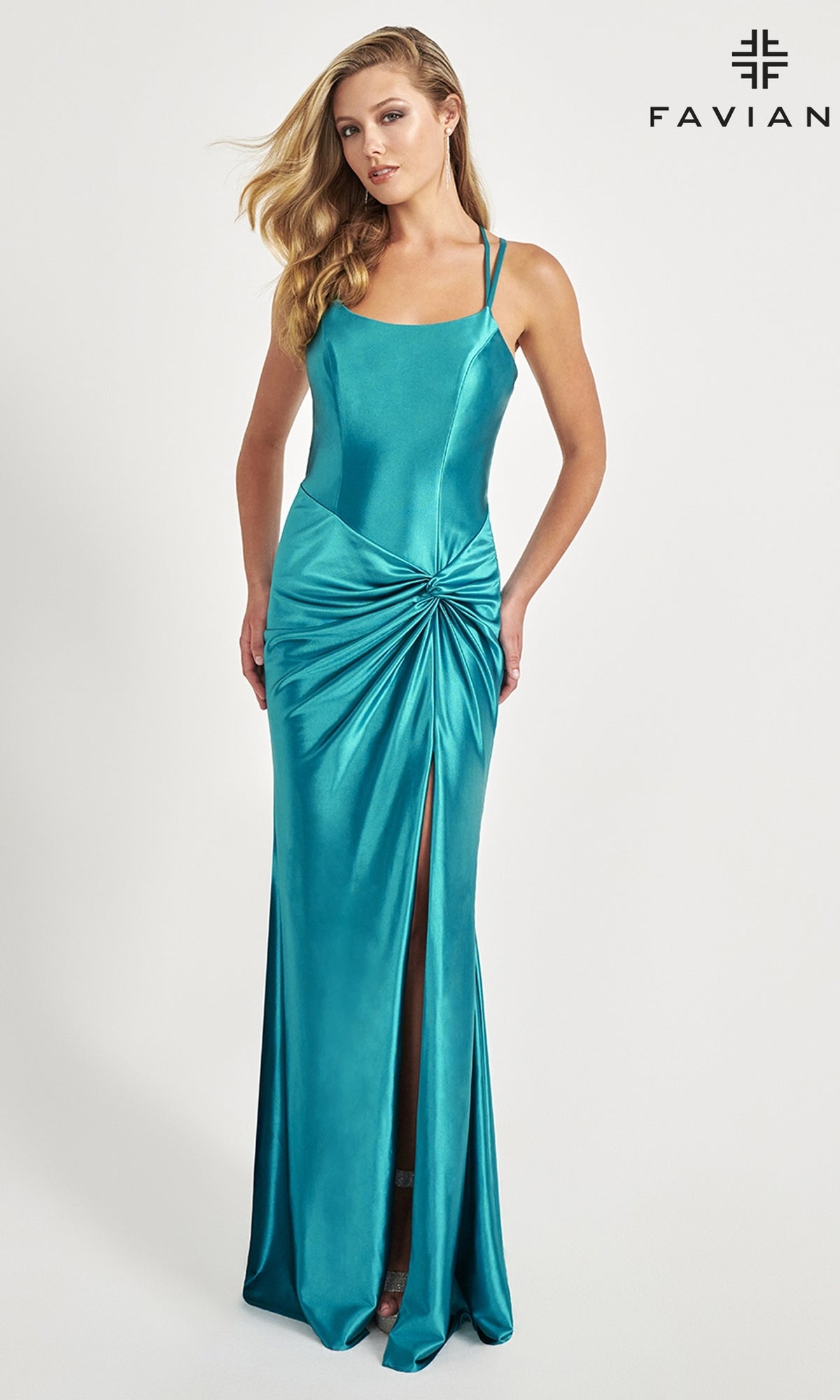 A woman models the Faviana Twist-Front Long Formal Dress 11024 in teal stretch satin, featuring a front slit and gathered knot detail, standing against a plain background with the Faviana logo in the top right corner.